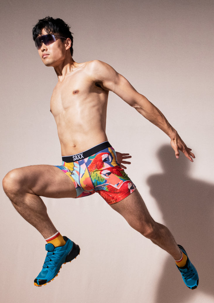 Man jumping while wearing sunglasses and boxer briefs in colorful parrot print