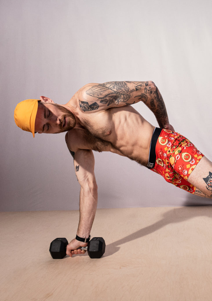 Man doing one arm push up while wearing red boxer briefs and yellow baseball cap